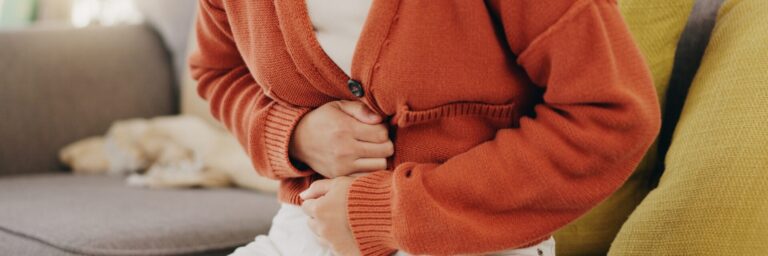 Stomach ache, cramps and hands of woman with abdomen pain due to constipation, menstruation or ibs issue. Sick, home and person suffering and holding belly in a house lounge, couch and living room.