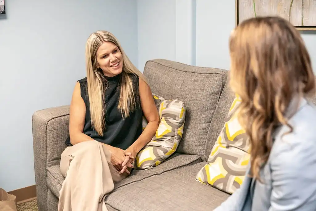 A young woman gets counseling from an older woman while they both sit relaxed on a couch.